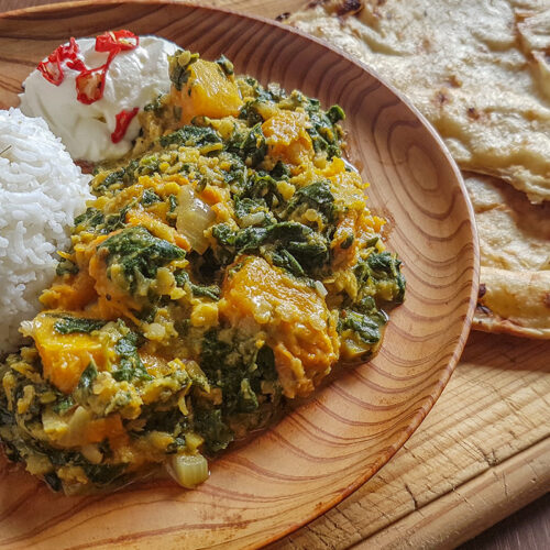 Dans une assiette en bois, une boule de riz blanc à côté d'un mélange de mauve et de potiron et d'une cuillère de crème aigre, à côté de l'assiette un pain plat