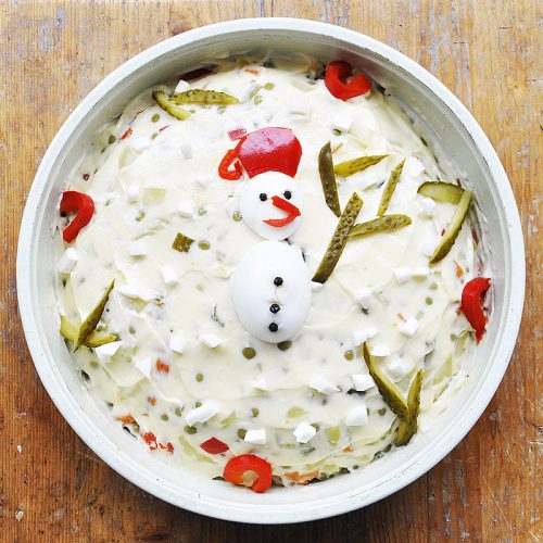 Salade Olivier fantaisie décorée avec des oeufs et des morceaux de poivron formant un bonhomme de neige